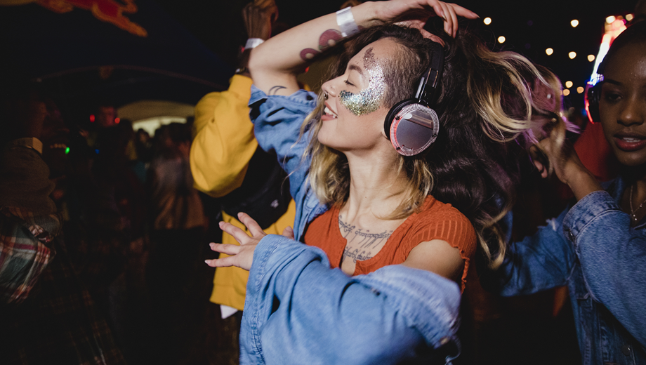 Girl with a glitter image on her face, dancing at a silent disco with headphones on.