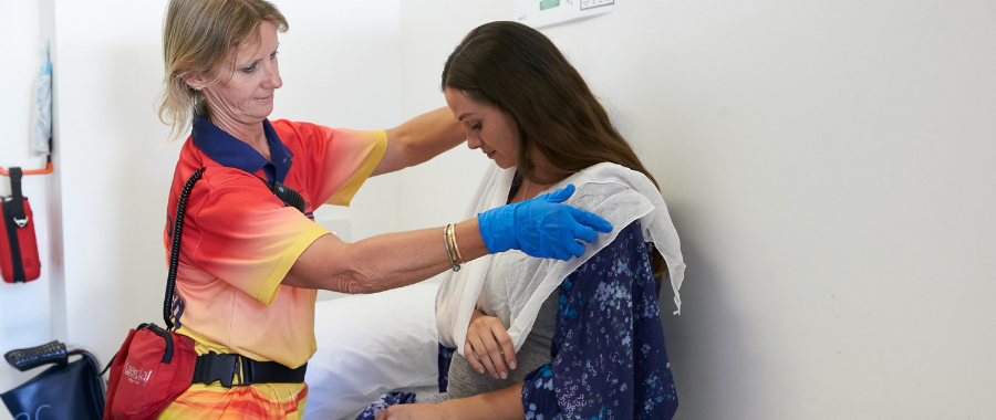 Lifeguard administering first aid by fitting a sling to a woman's arm