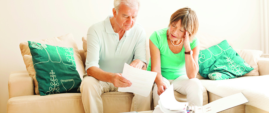 an older couple sitting on the couch looking at paperwork visibly overwhelmed.