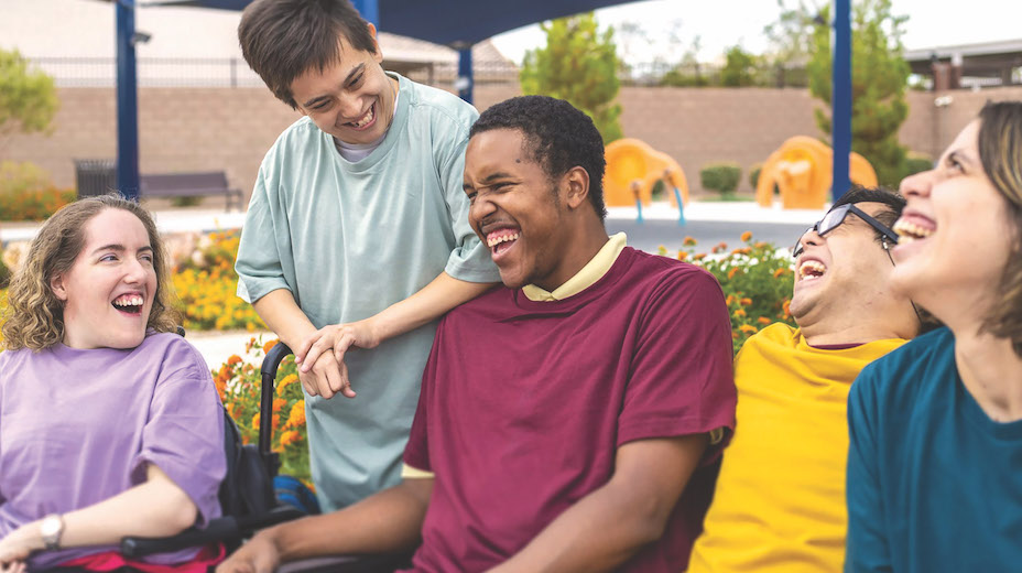 Five young adults laughing. One person is sitting in a wheelchair.