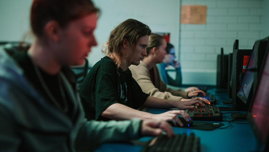 A teenage girl sitting at a computer typing on a keyboard with other teens sitting at computers beside her in the background.
