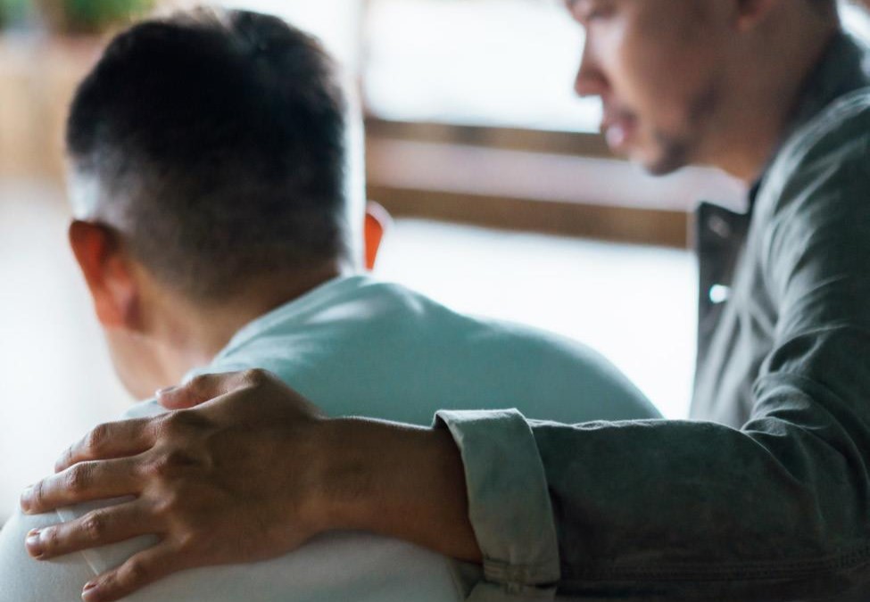 man with arm over another man shoulder for comfort