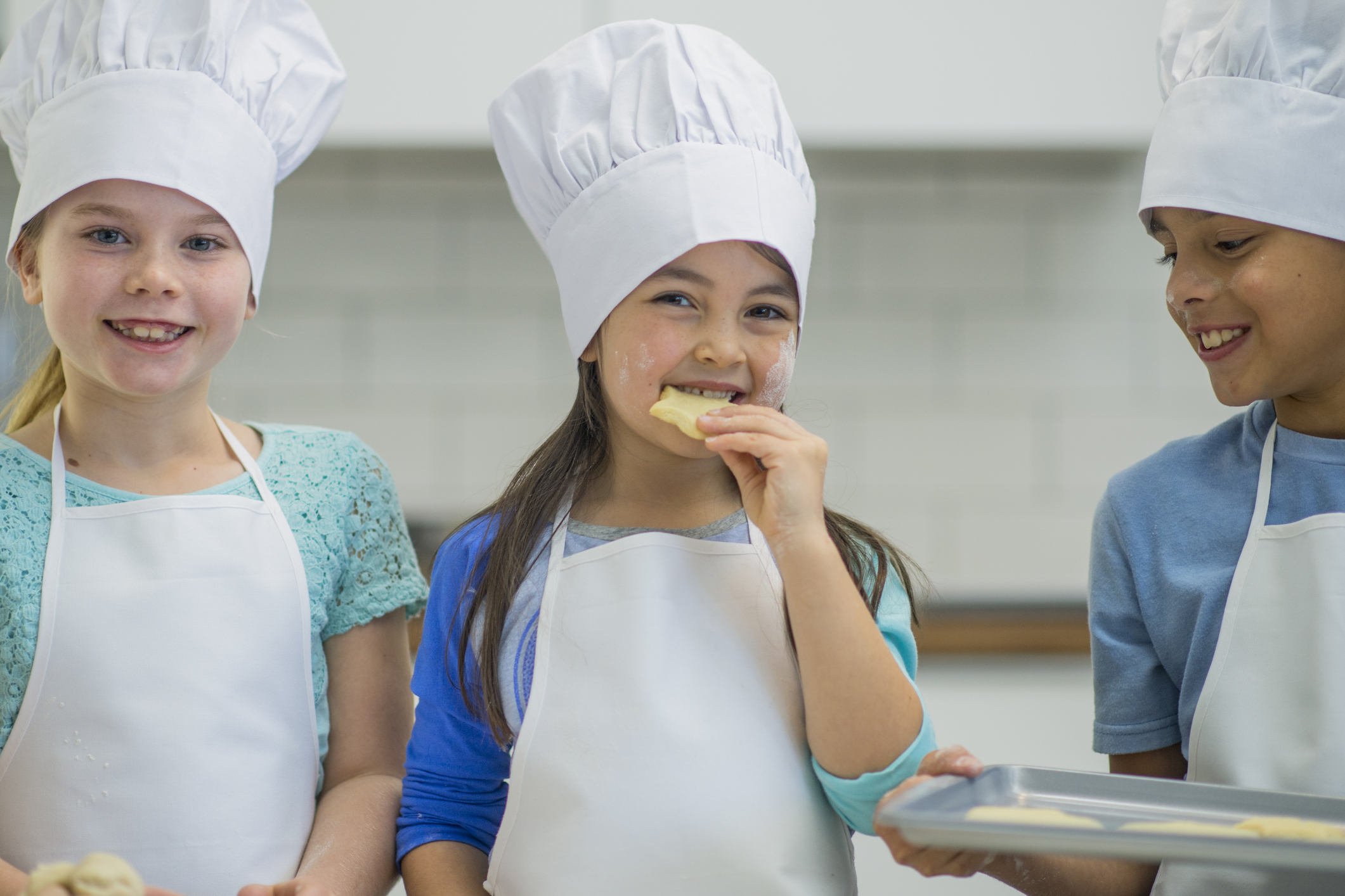 3 Children in chefs hats in a kitchen ready to cook 