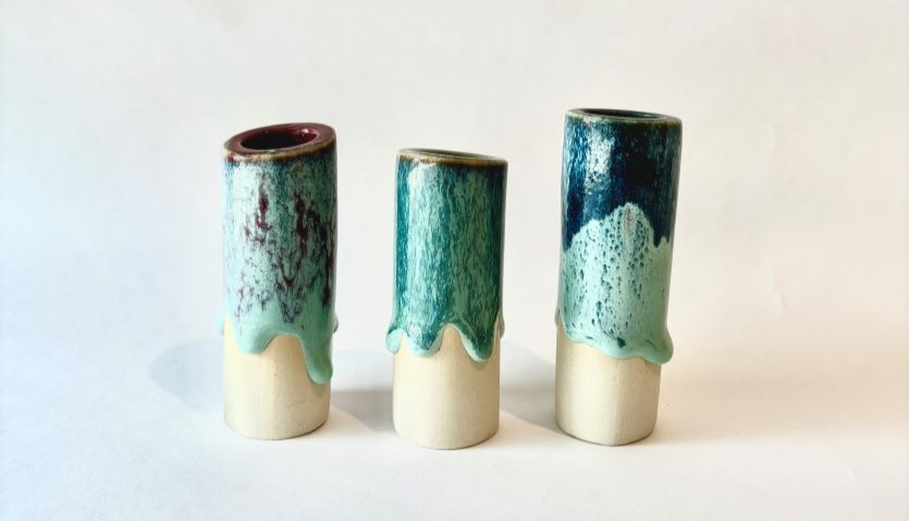 three cylindrical ceramic vessels sit on a white background. They are cream on the bottom, with a shiny blue glaze appearing to drip from the top.