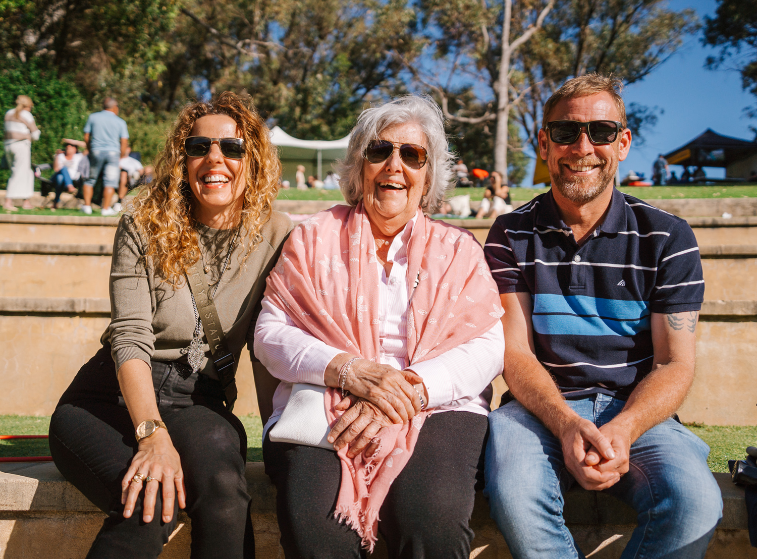 Three people sitting on a limestone step at a local park, all smiling at the camera