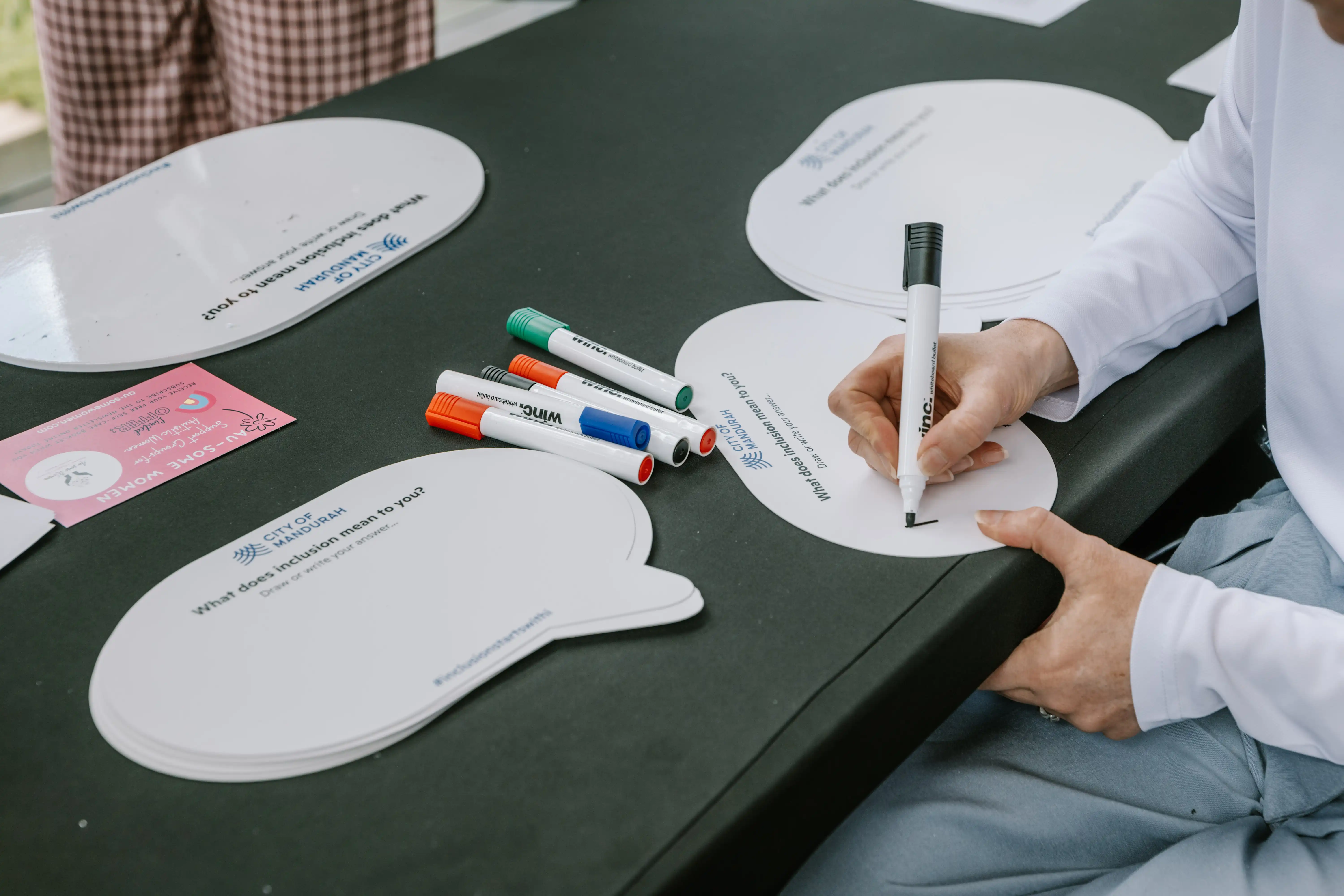 Person writing their thoughts on a speech-bubble card during a City of Mandurah community consultation activity about inclusion.