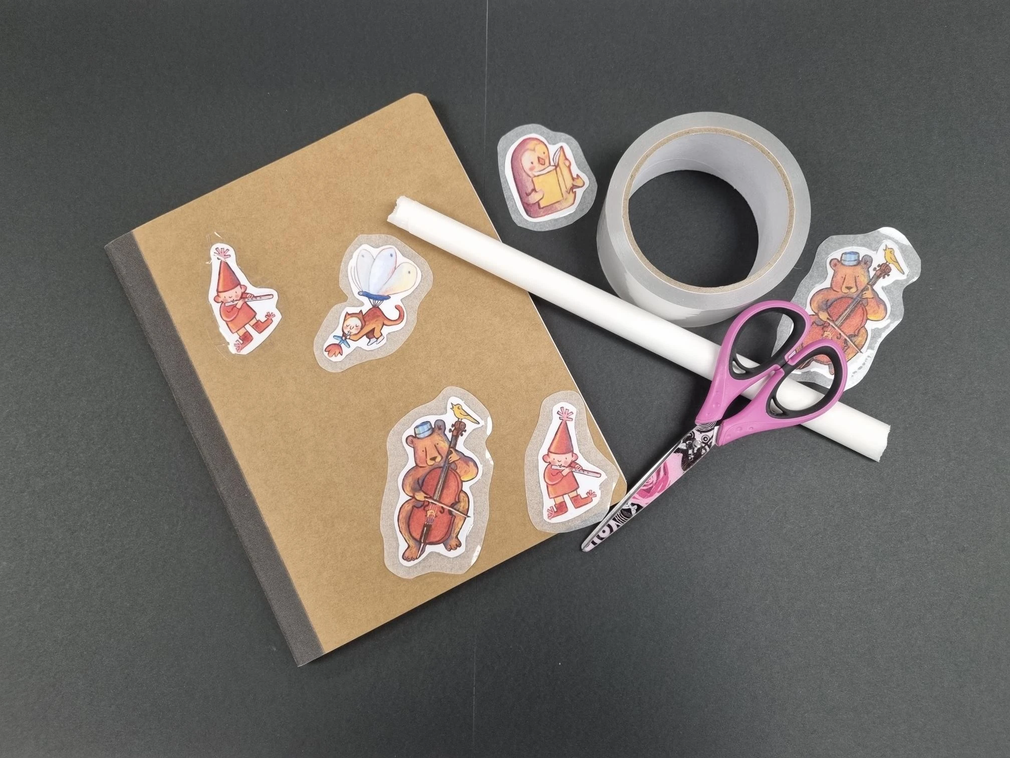 Homemade stickers lying on top of a cardboard book with sticky tape and scissors next to them.