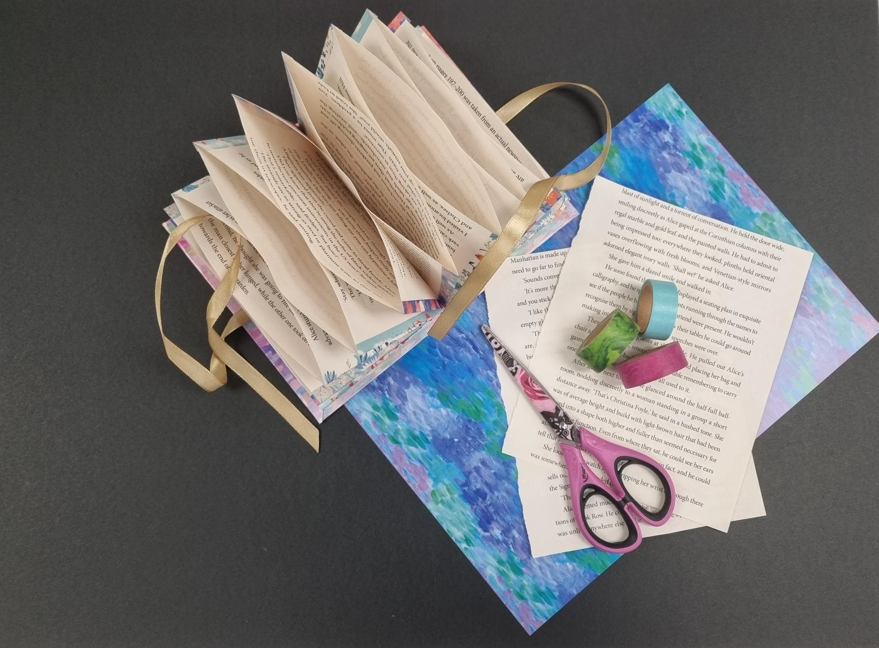 A book that has been made into an accordion with extra pages, scissors and craft materials lying next to it.