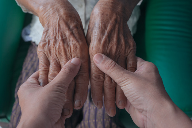 An older perons hands being held by a younger persons hands.