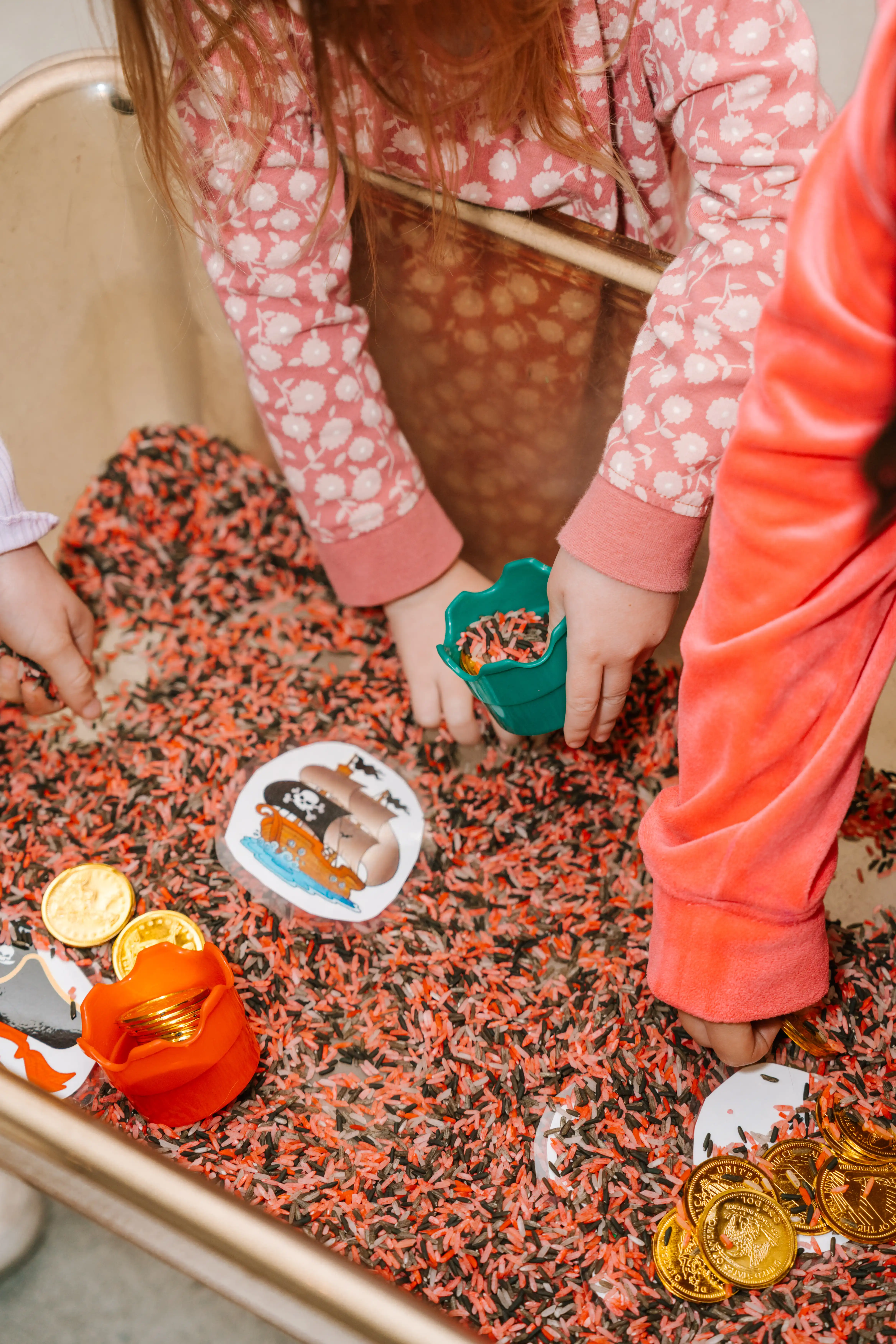 Child scooping toy coins from a sensory play tray at the MARC crèche