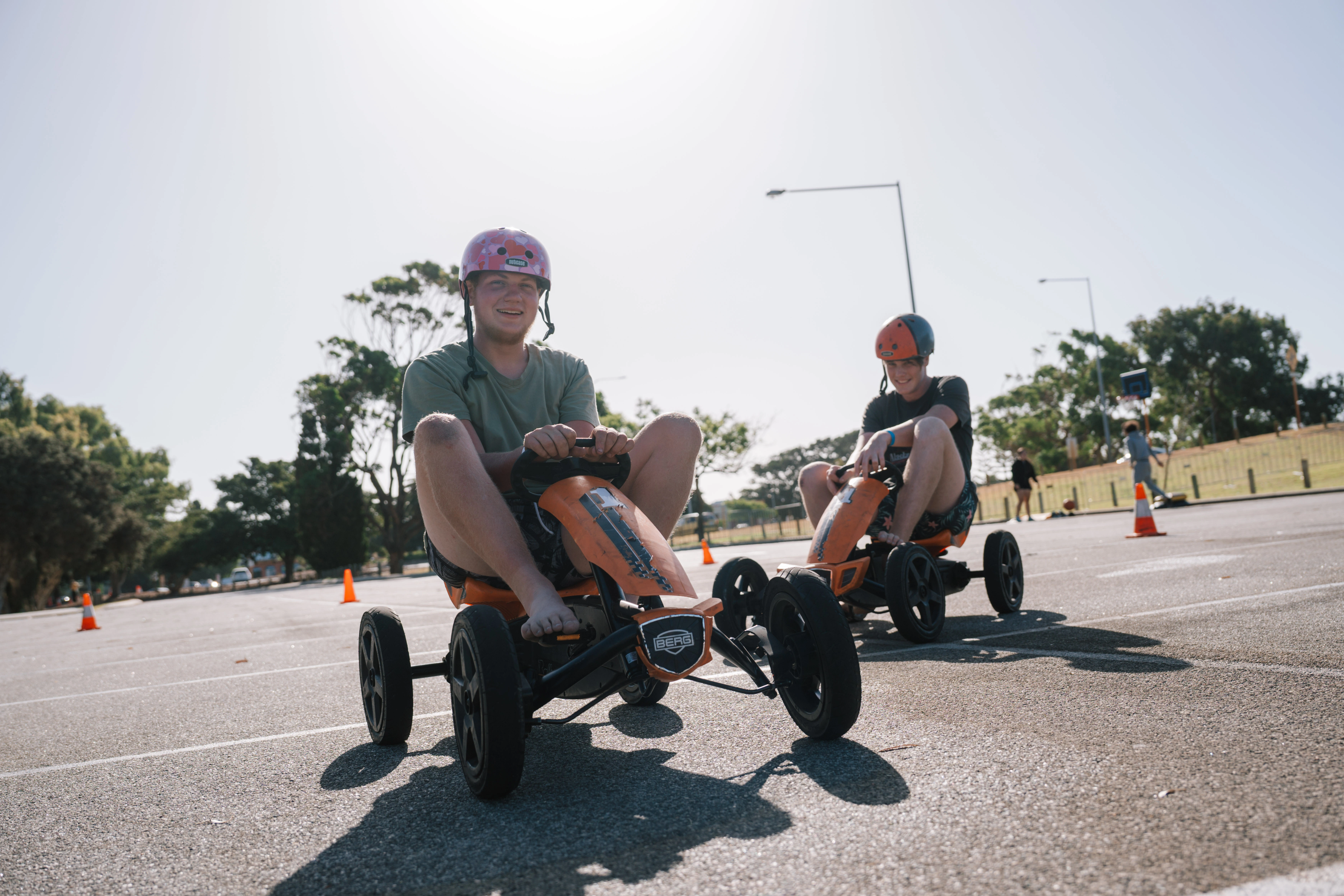 Two teenage boys sitting on karts, smiling at the camera with helmets on.