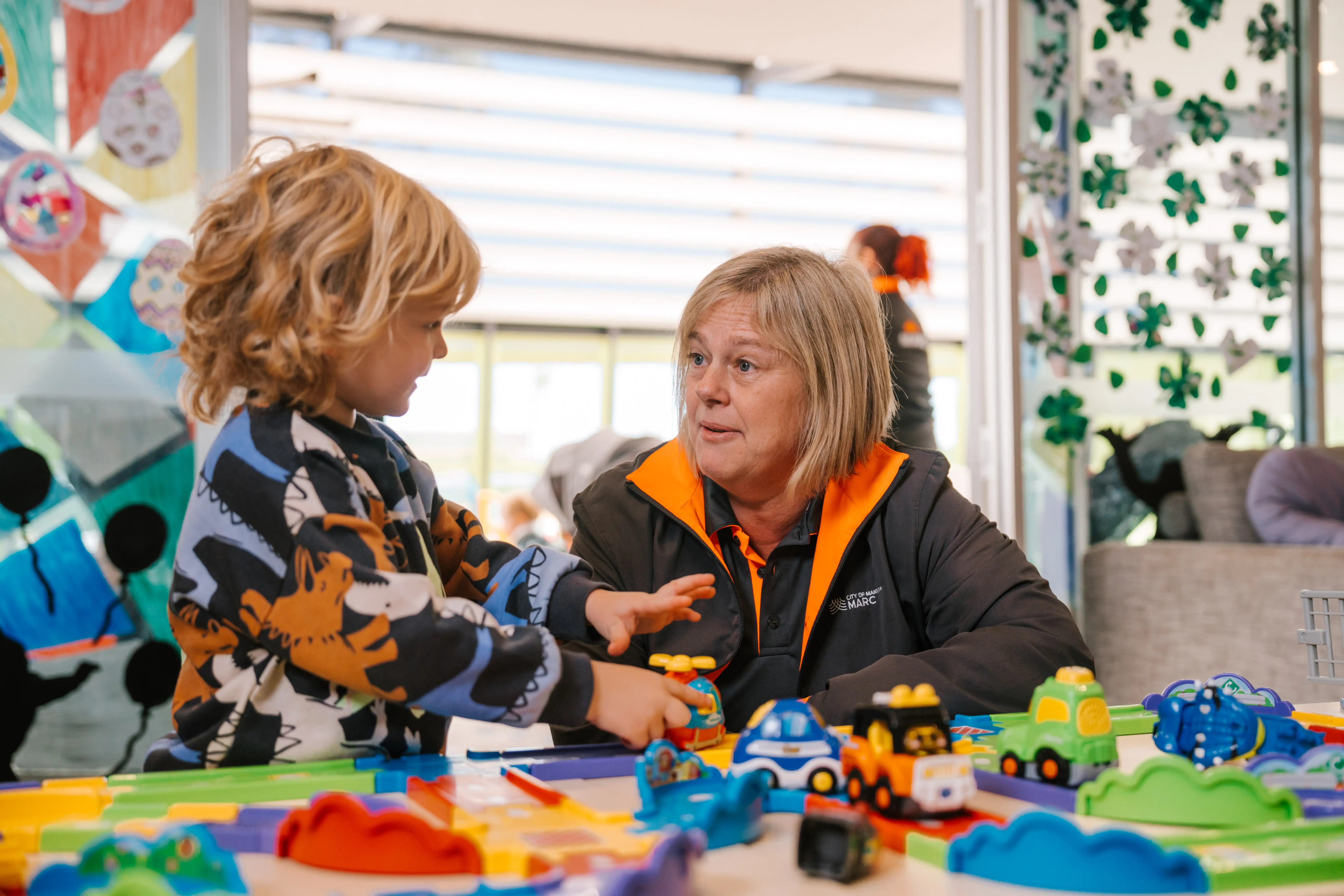 Carer playing with toy vehicles with a child at the MARC crèche