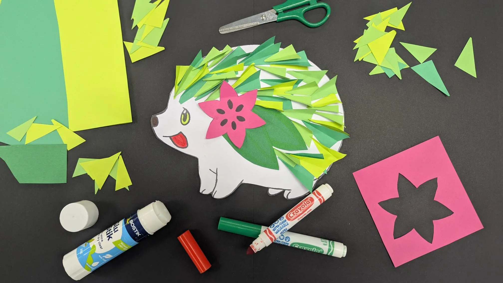 Craft Pokemon Shaymin character lying on a black background with glue, textas and craft paper lying around it.