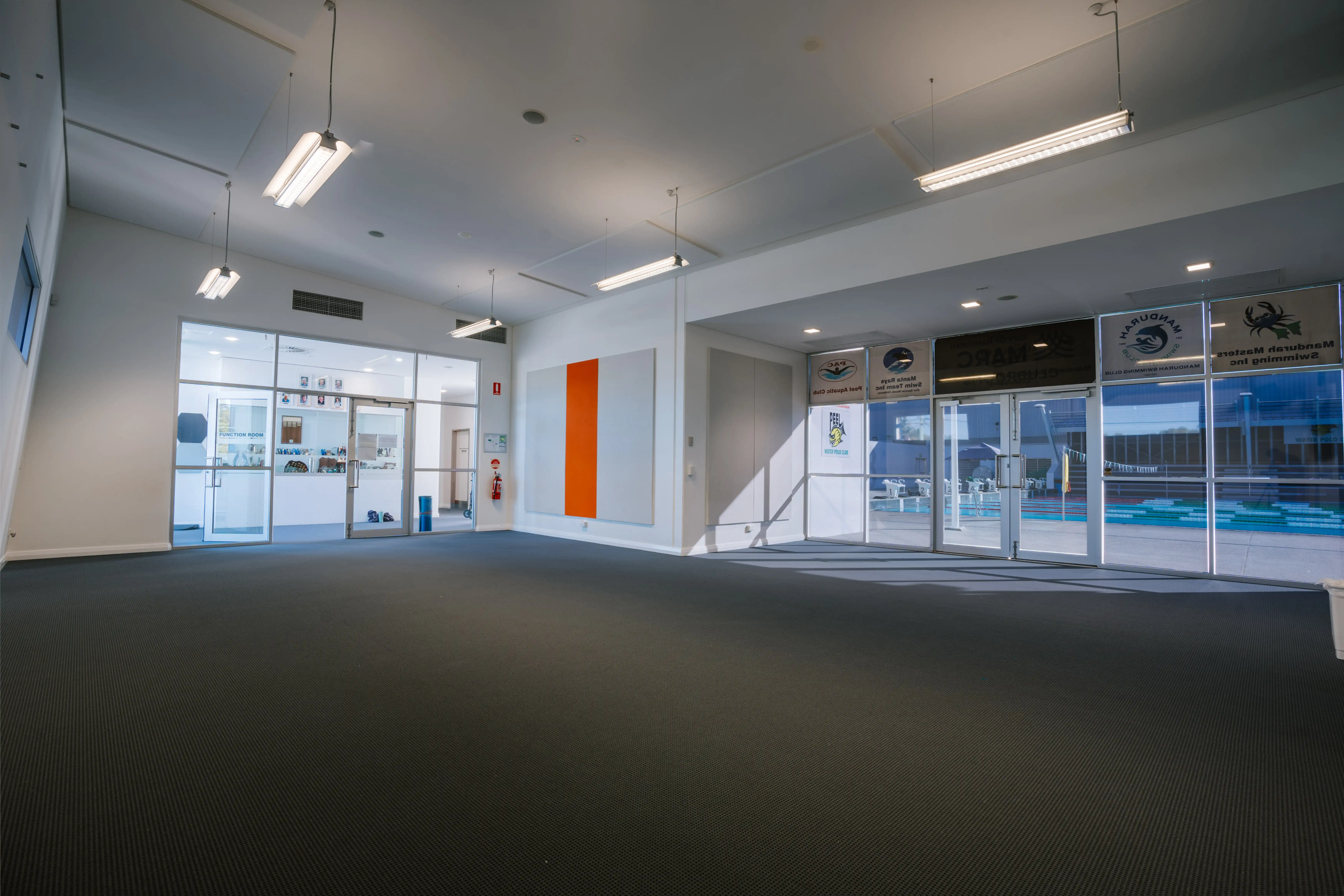 Spacious Swim Club Room at MARC with carpet flooring and poolside glass walls.